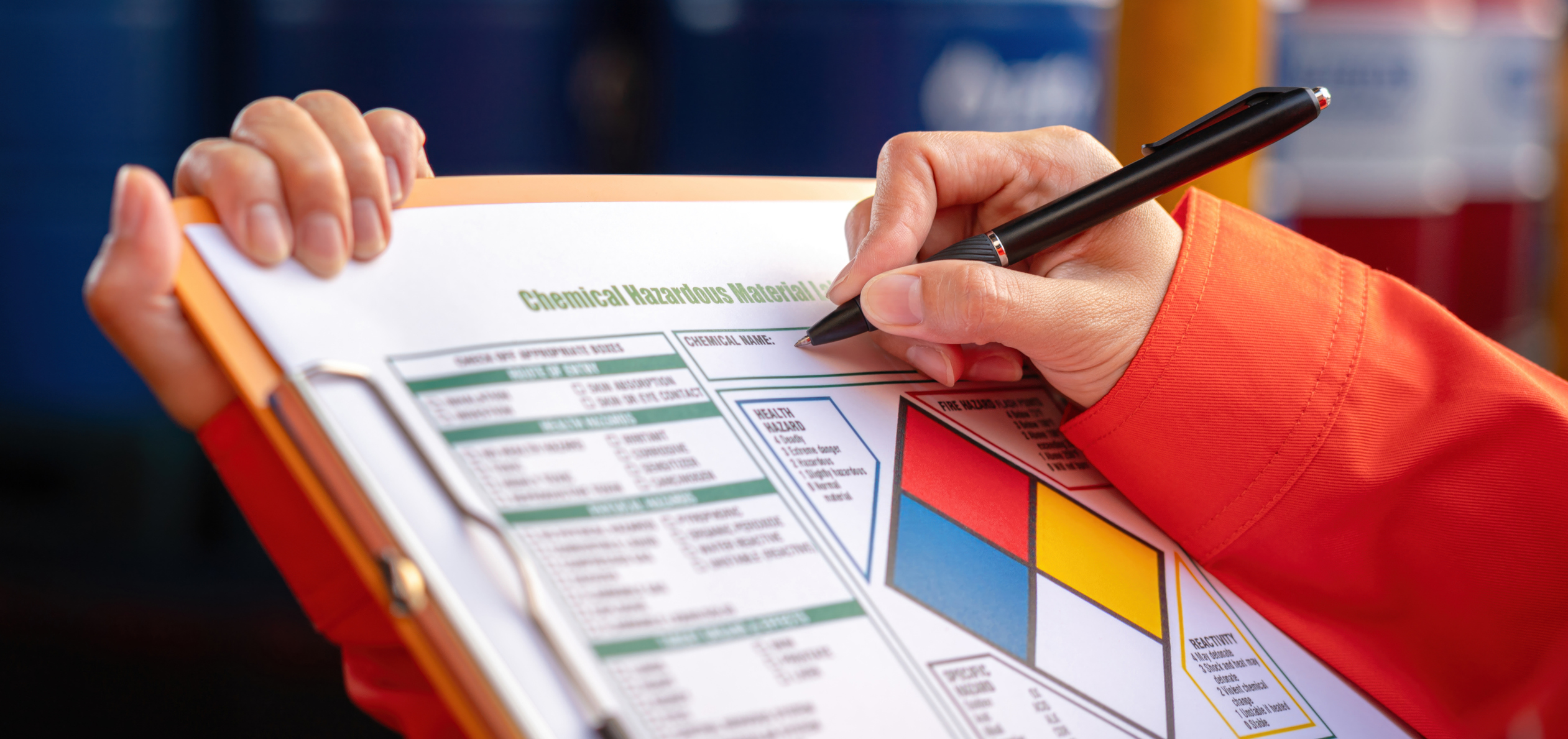 Extreme close-up at industrial worker's hand during verify on chemical and hazard material checklist, with background of chemical storage place. Industrial working with safety practice scene.