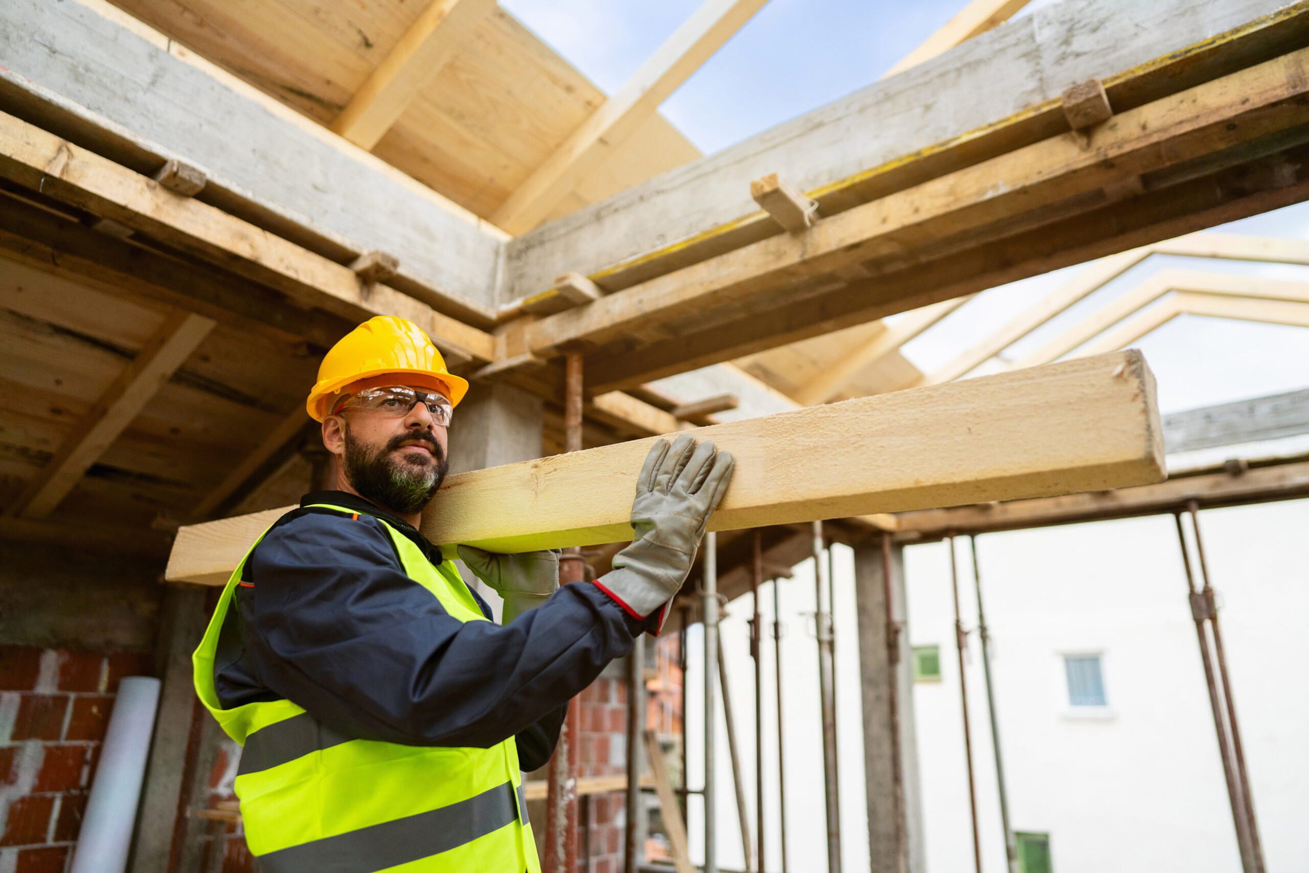 Mid-adult male Caucasian roofer, carrying a big timber, while working on a rooftop, making a roof beam